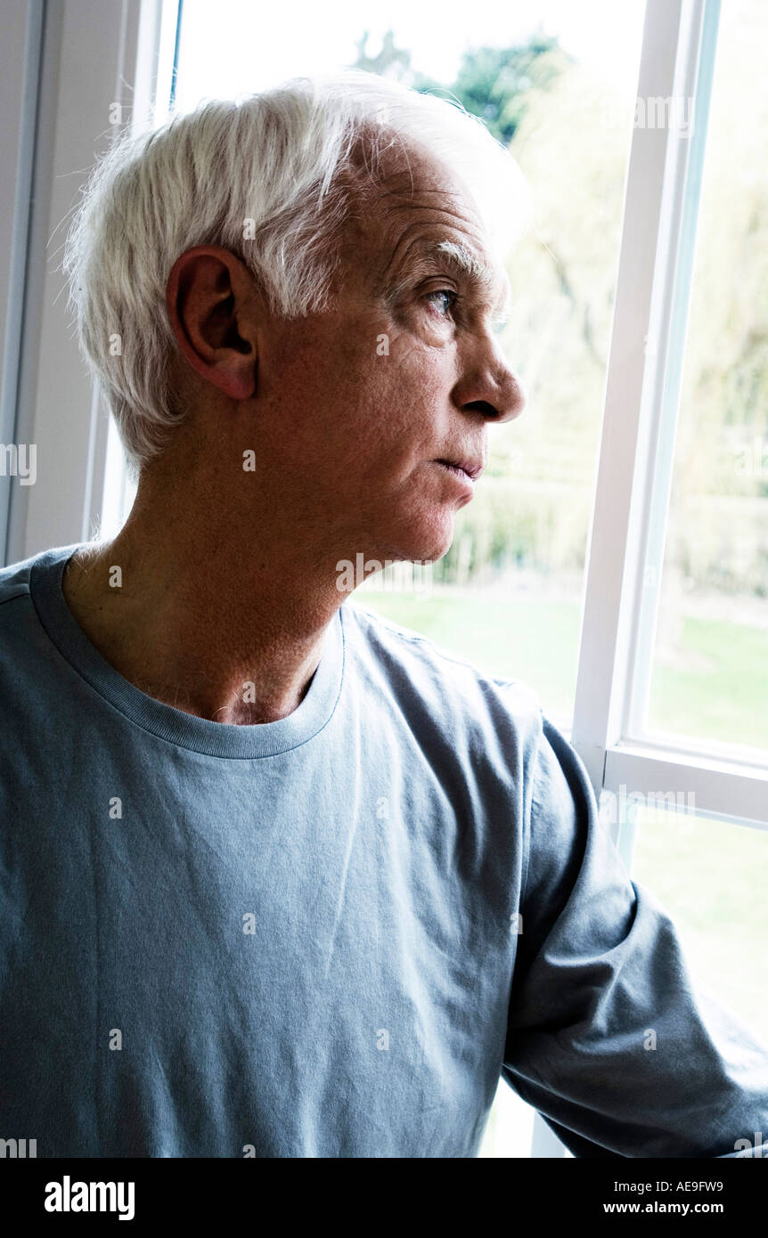 Thinking senior man looking through a window Stock Photo