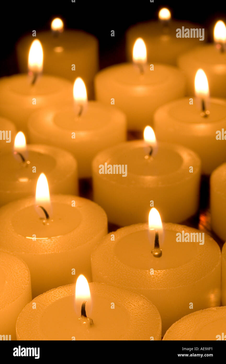 tea light candles grouped together lit against dark background one coloured orange reflective illumination natural candlelight o Stock Photo