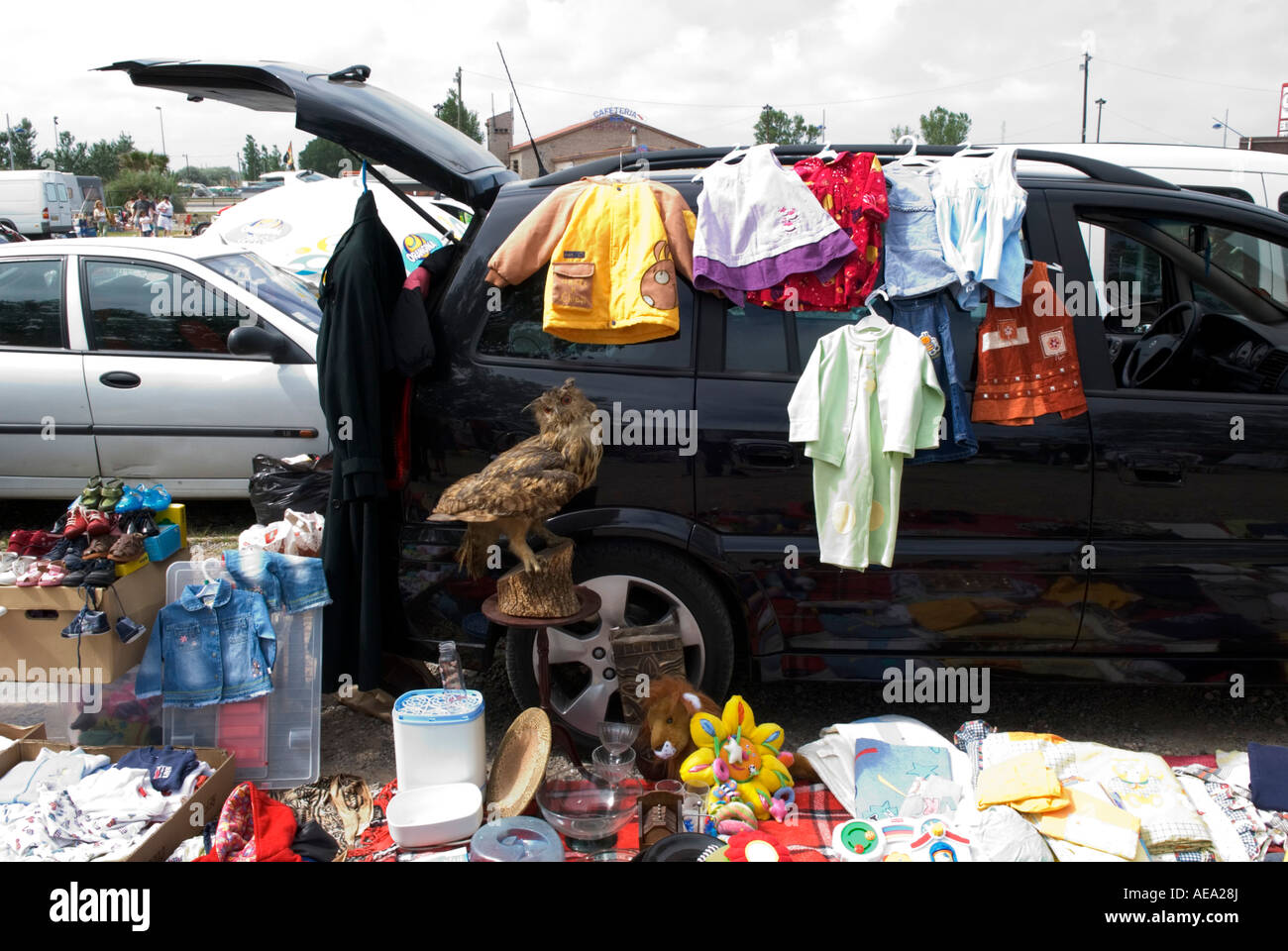 a stuffed eagle owl sits amongst a pile of junk in front of car at a french flea market Stock Photo