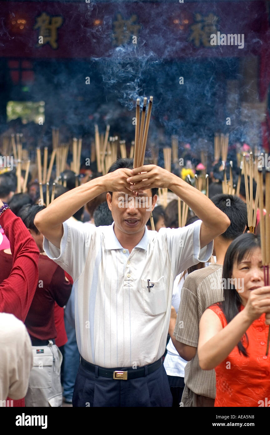 A Chinese man holding burning incense sticks in front of a praying ...