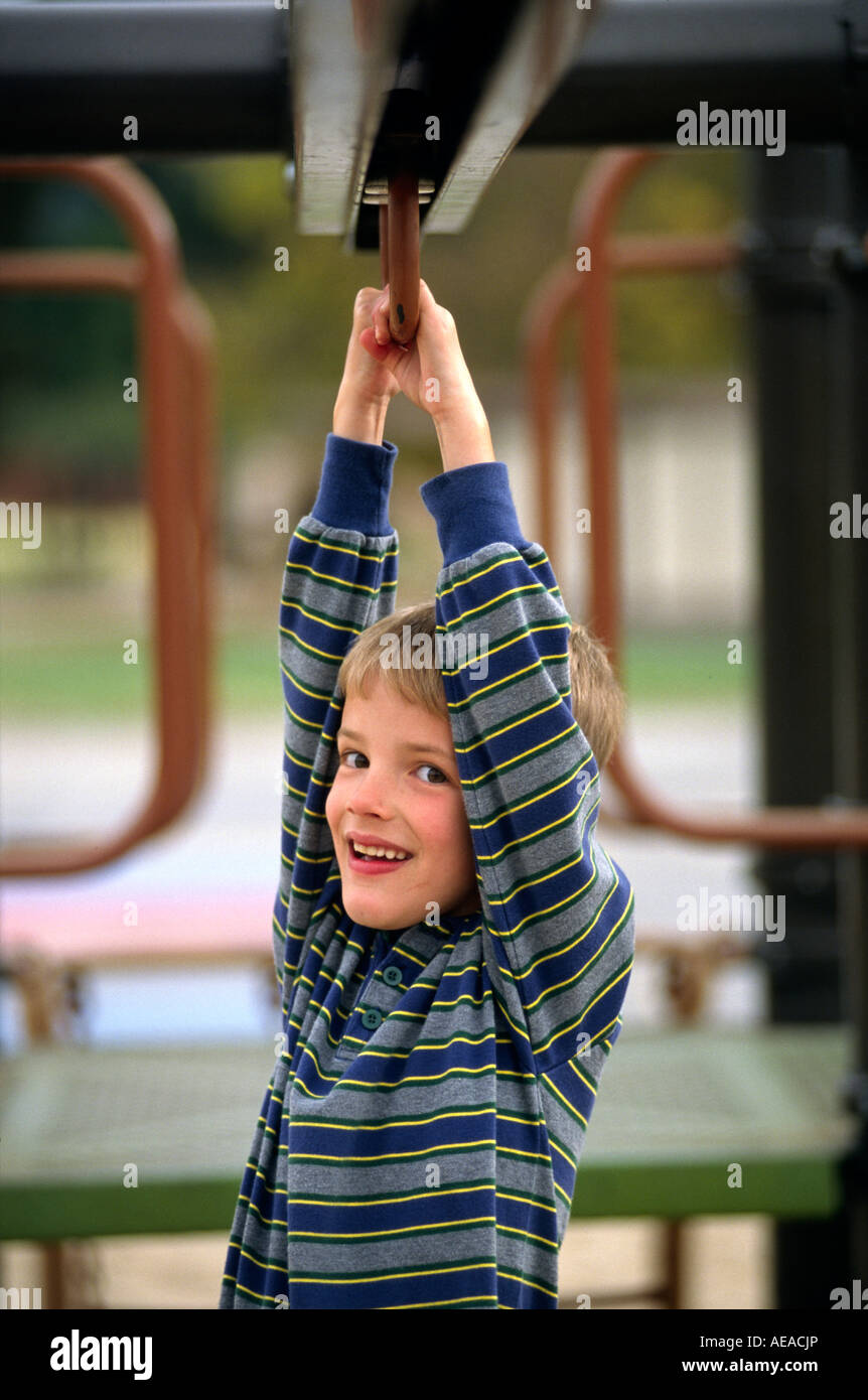 A seven year old BOY plays on the playground bars Stock Photo