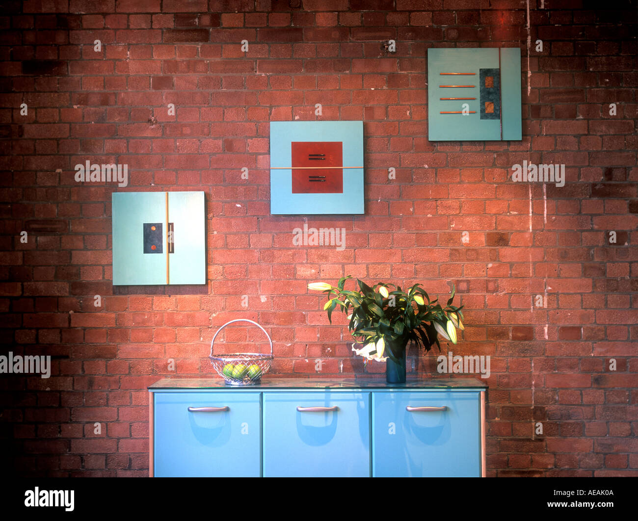 modern warehouse conversion apartment showing blue cabinet with vase of lilly flowers and 3 three picture hanging on red brick w Stock Photo