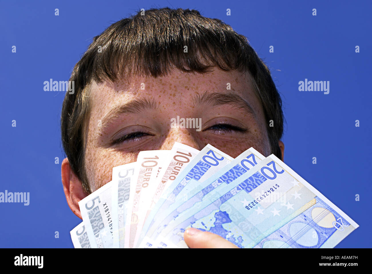 Irish boy holding up Euro bills against clear blue sky Stock Photo