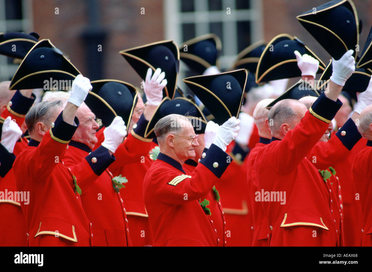 Chelsea Pensioners in red jackets raise their tricorn hats and cheer on