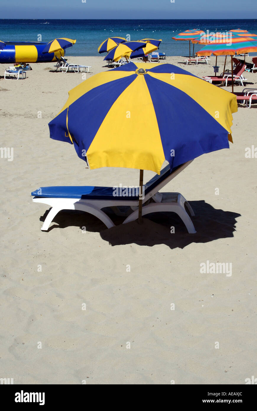 A COLOURFUL SUNBED AND UMBRELLA STANDING ON A SANDY BEACH. MALTA