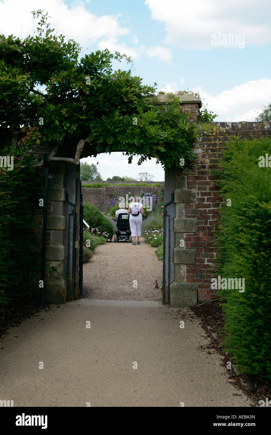 Woman accompanying man on mobility scooter visiting public gardens in Sussex, England, UK Stock Photo