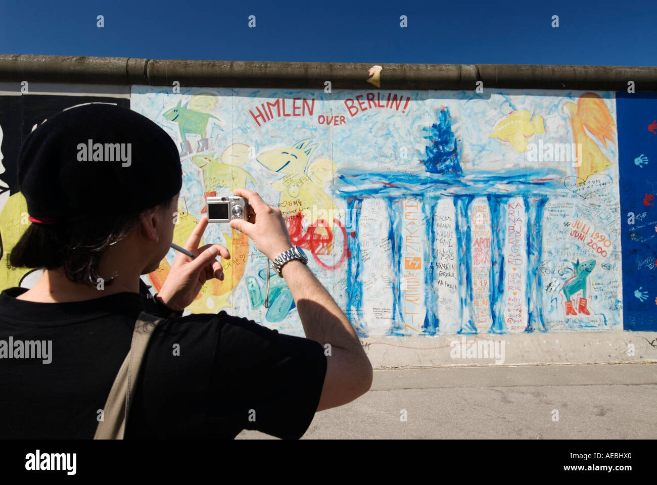 Tourist photographing mural of Brandenburg Gate on Berlin Wall at East Side Gallery Berlin Stock Photo