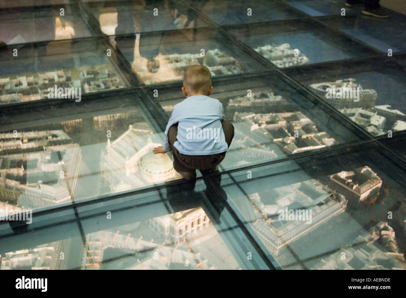 young boy crouched and looking through a glass floor at a scale model plan for L Opera in the Musee D orsay in Paris France Stock Photo