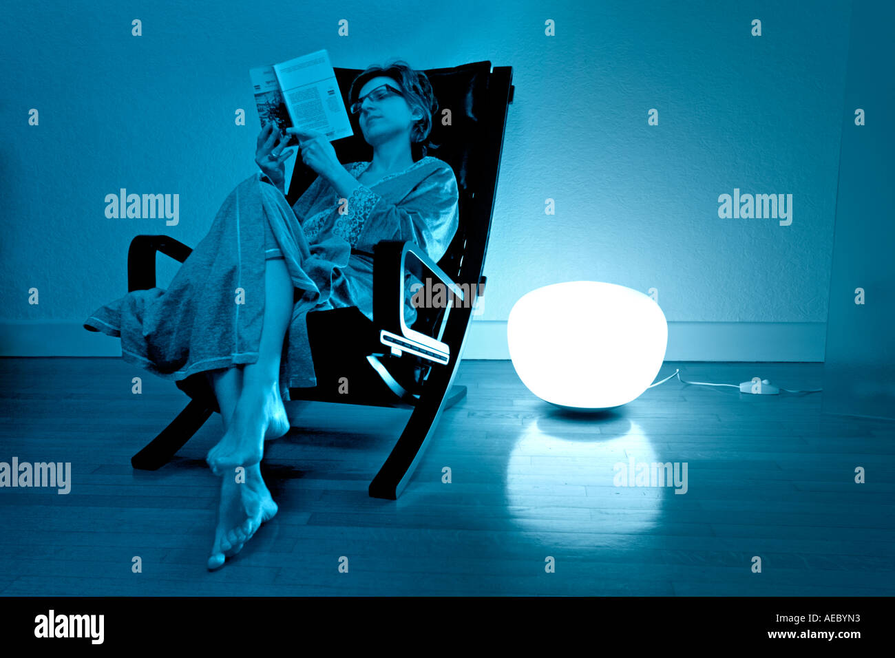 In a blue atmosphere, reading cocooned in the bosom of an armchair. Lecture confortable en ambiance bleue. Stock Photo