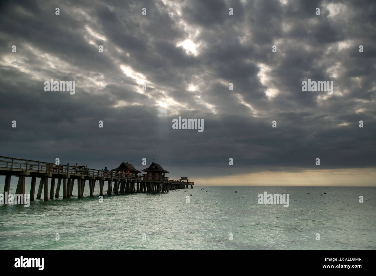 The old wooden pier at Naples beach with dramatic stormy sky and shafts of sunlight over the sea Stock Photo
