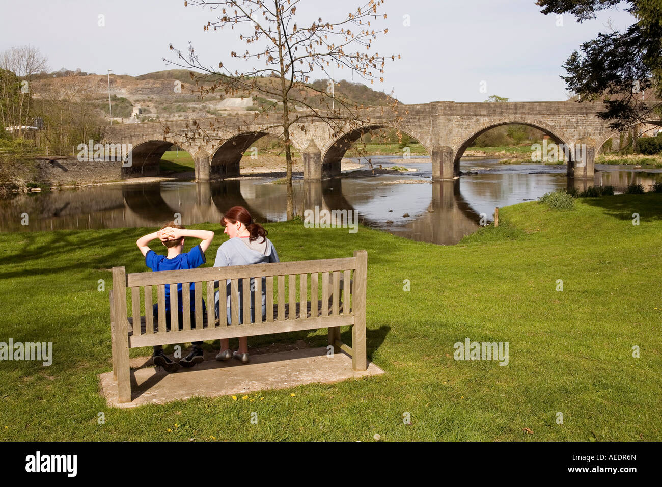 UK Wales Powys Builth Wells two people on bench by bridge over River Wye Stock Photo