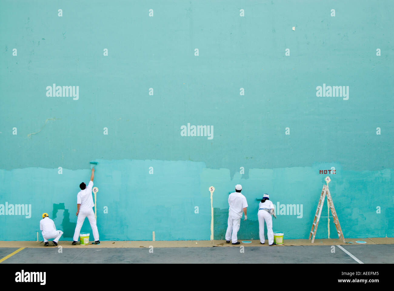 Team of workers painting large blank wall turquoise for game of pelota, Spain Stock Photo