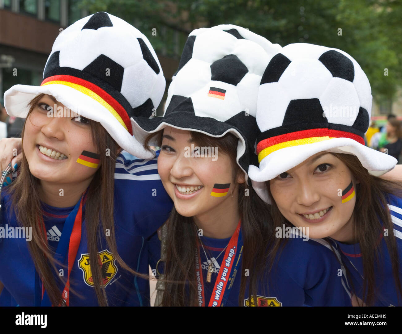 Three female Japanese football fans in good mood posing with hats and stickers in German national colours Stock Photo