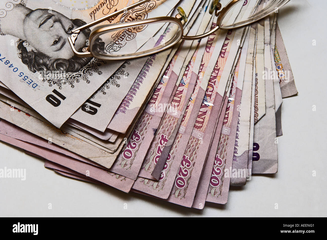 Stack of used British banknotes mixed denominations with metal framed glasses on top Stock Photo