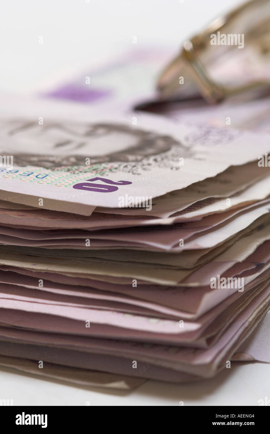Stack of used British banknotes mixed denominations with metal framed glasses on top Stock Photo