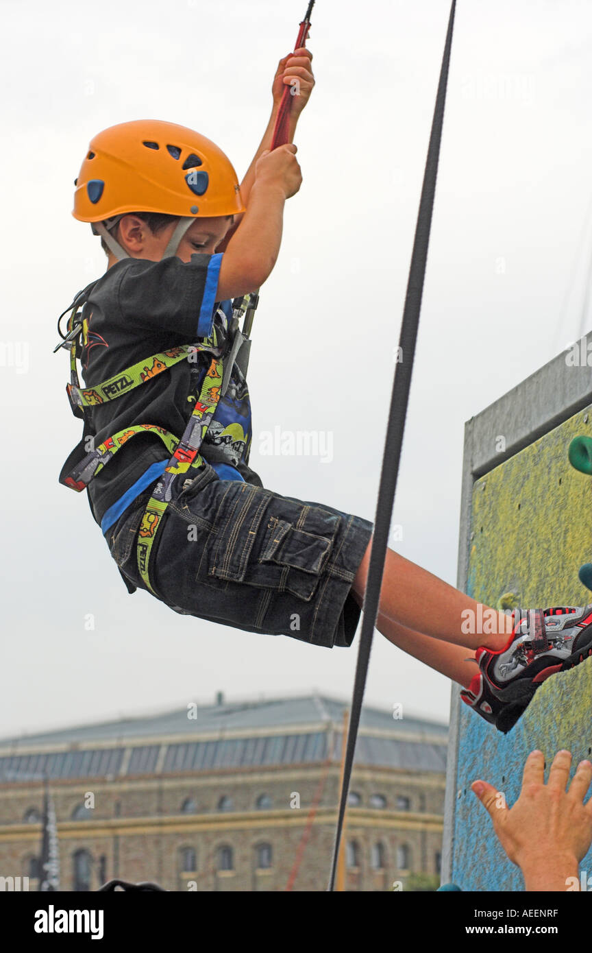 Young boy on climbing wall rappelling down with instructors hand ready to help Stock Photo