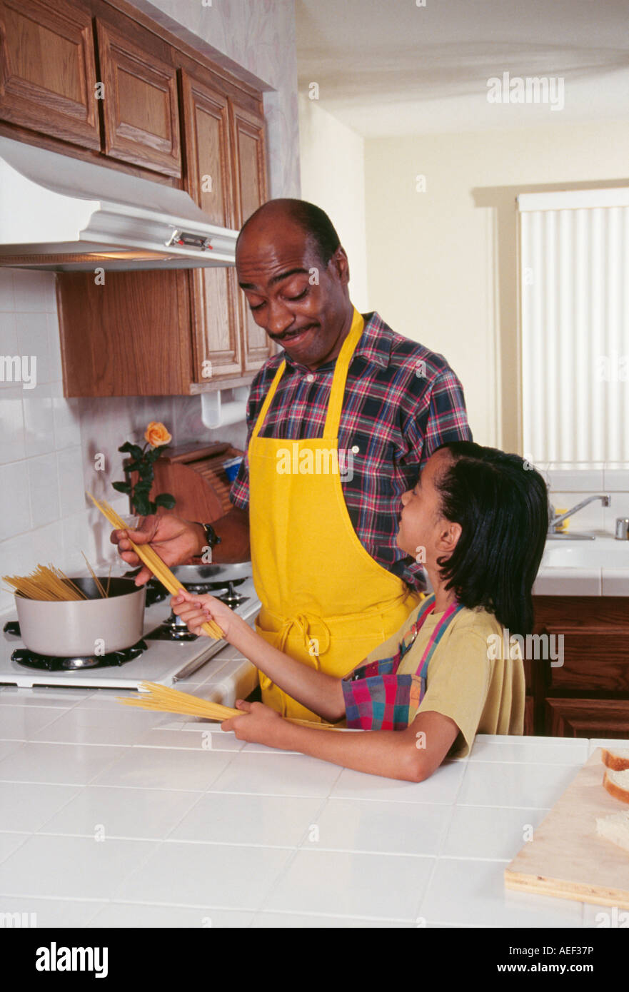 Dad and daughter working in 7-9 year old preparing pasta spaghetti dinner meal kitchen diverse diversity looking at each other smiling smile smiles POV  MR Stock Photo
