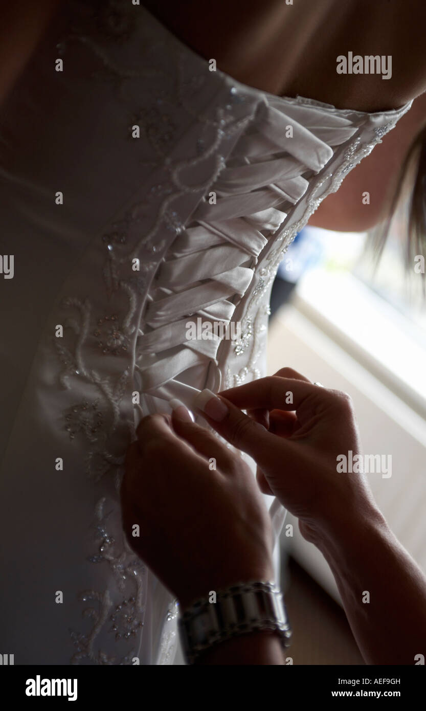 bride being helped to lace up her wedding dress by bridesmaid with long nails Stock Photo