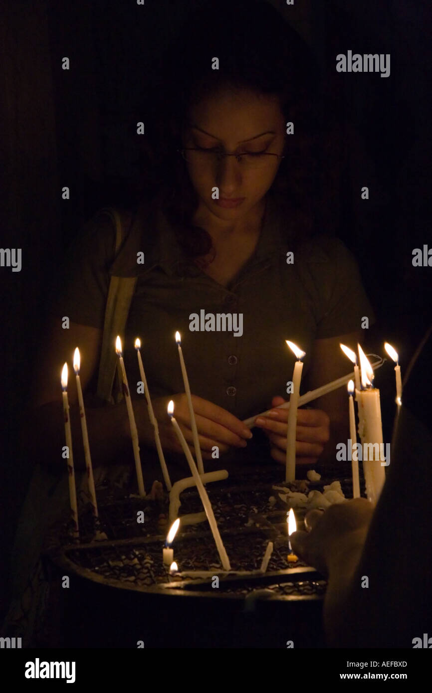 Stock photo of a young woman lighting candles in prayer in the Church