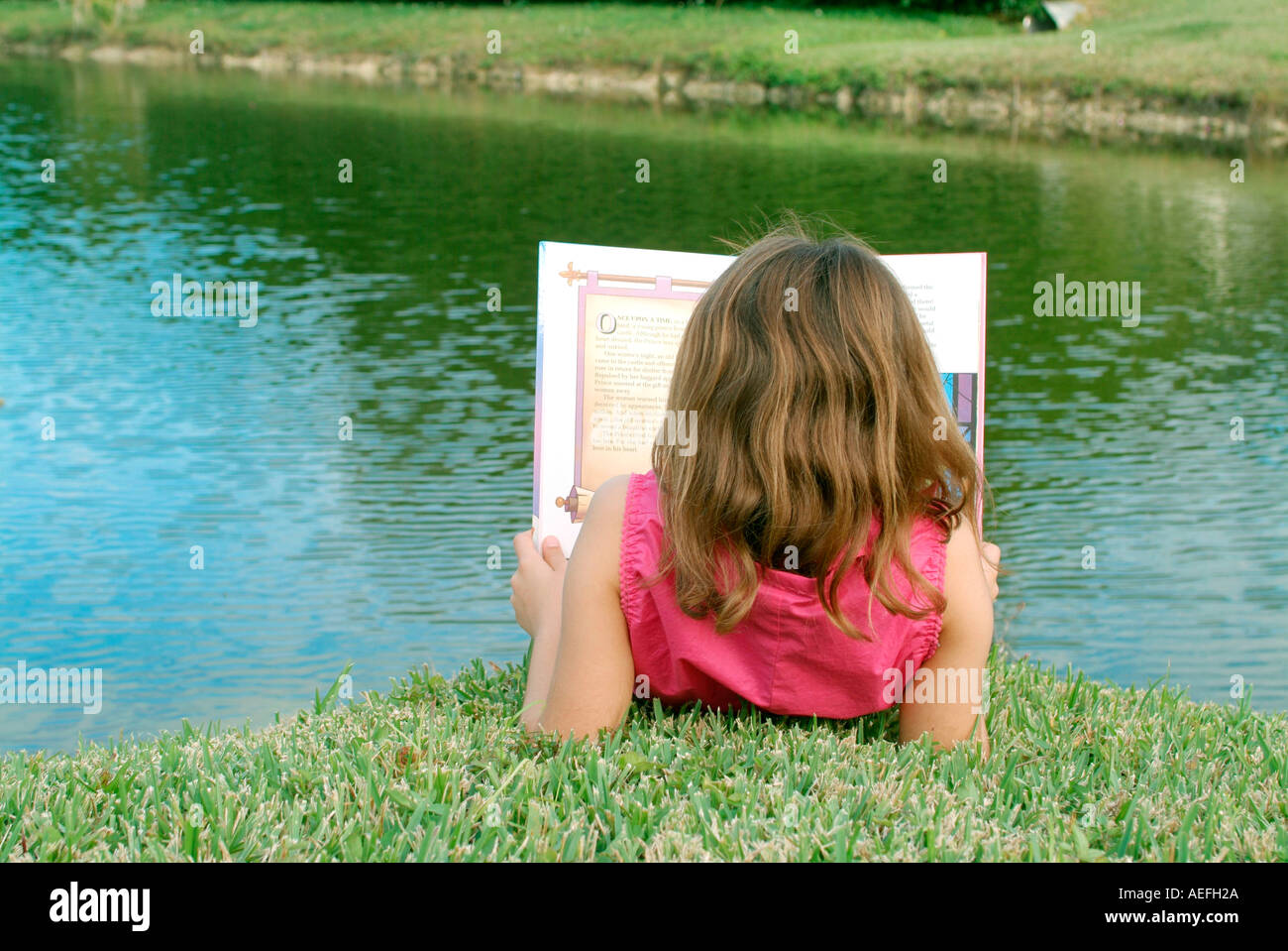 Little girl reading storybook near lake Stock Photo Alamy
