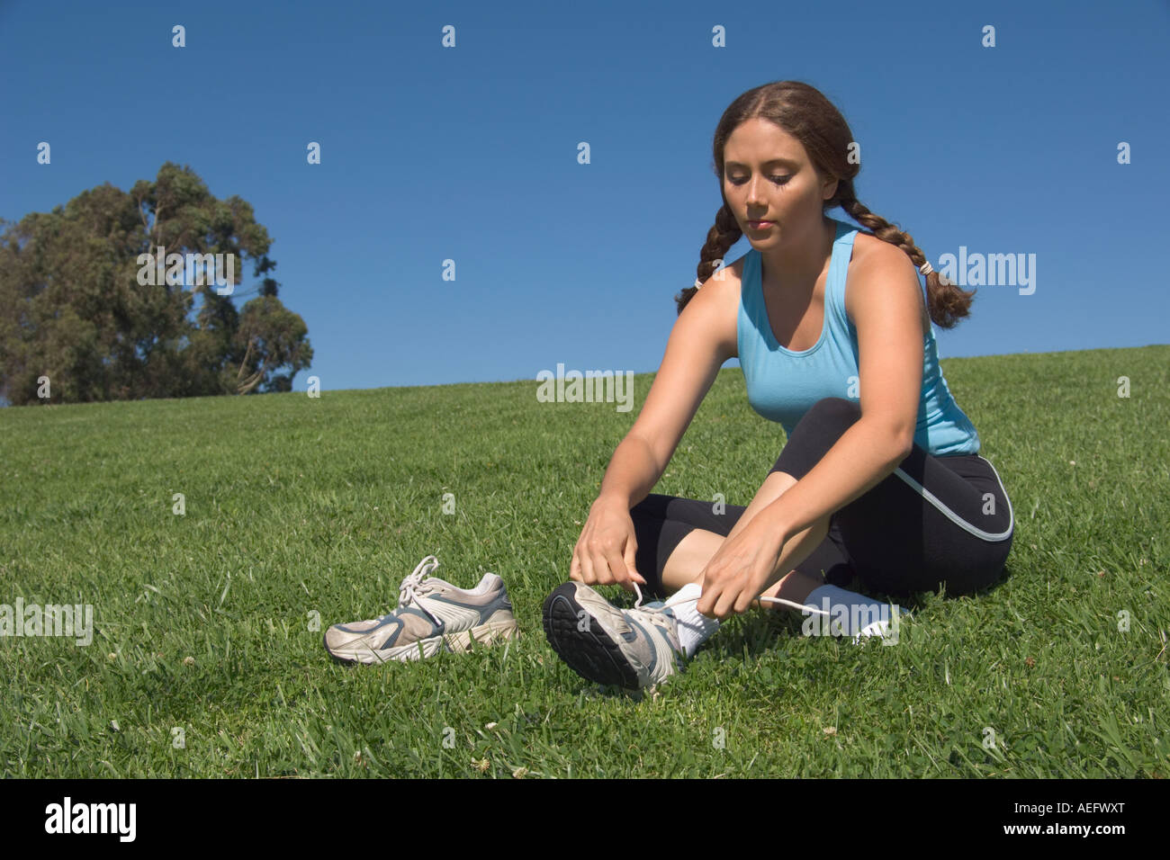 Young woman putting on athletic shoes in field Stock Photo Alamy