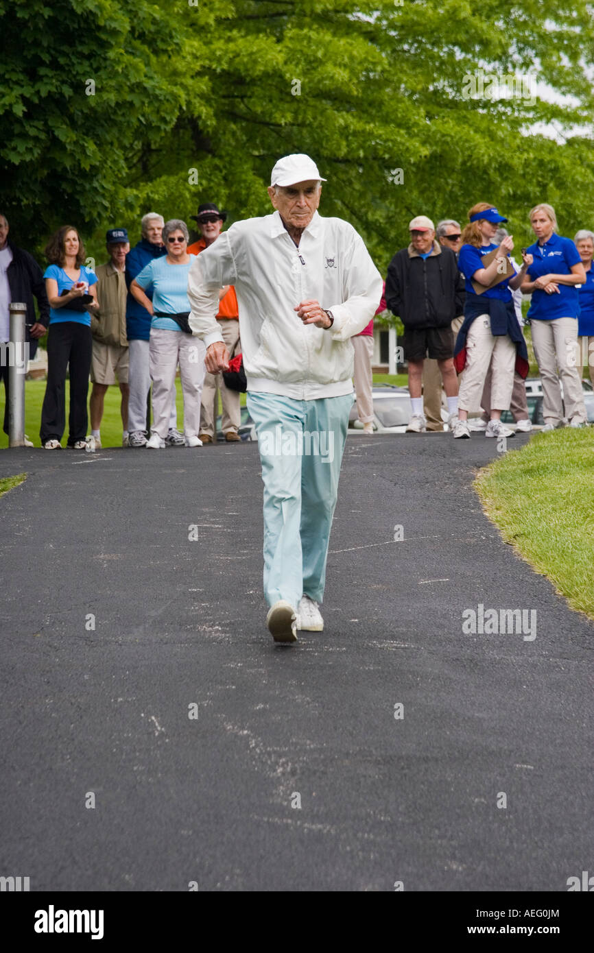 Elderly man starting his lap in a relay fast walking race as his teammates and competitors look on Stock Photo
