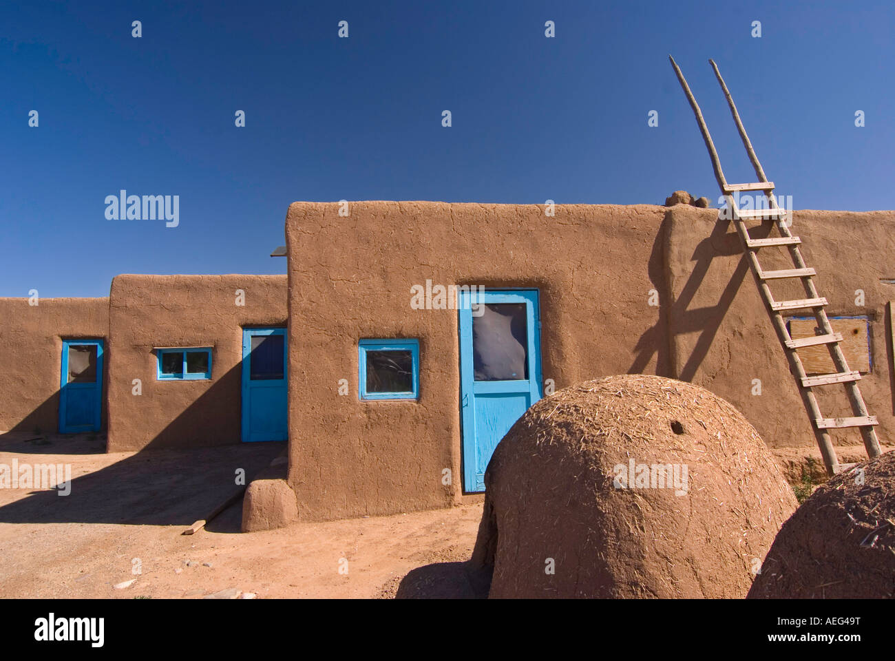 A bread oven and ladder in front of adobe dwellings in Taos Pueblo, Taos, New Mexico Stock Photo