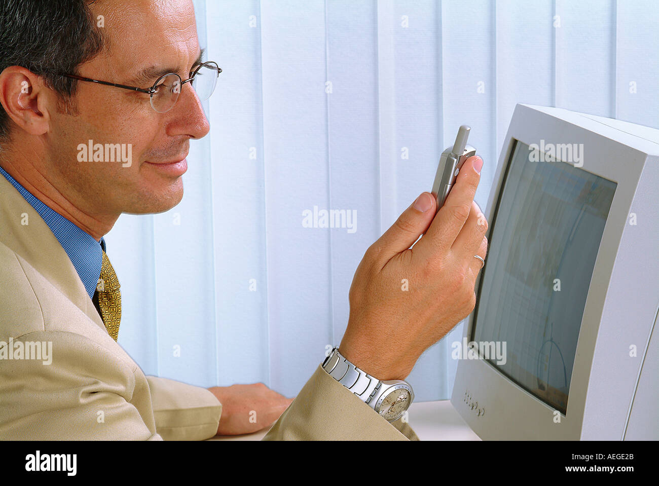 businessman sitting desk computer screen monitor watch cellphone cellular phone mobi blinds looking at business communication pe Stock Photo