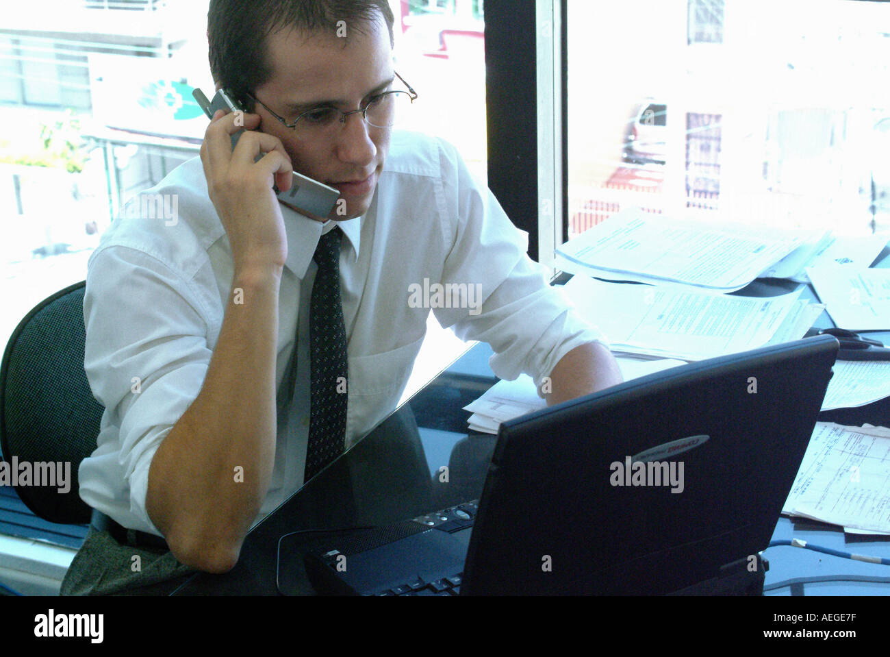 Businessman desk office laptop papers shirt tie glasses window cellphone cellular phone chair people communication business conc Stock Photo