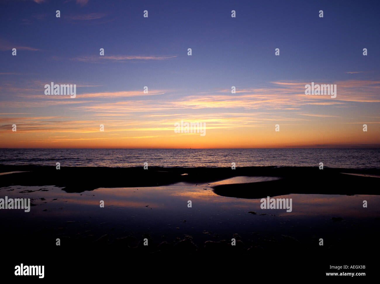 Wave rolling in on a sandy beach at sunrise with the tops of the wave just breaking and catching the sun s rays from behind Stock Photo