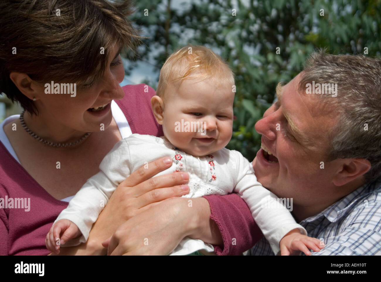 Horizontal close up portrait of a young family, (mum, dad and six-month old first-born daughter) in the garden. Stock Photo