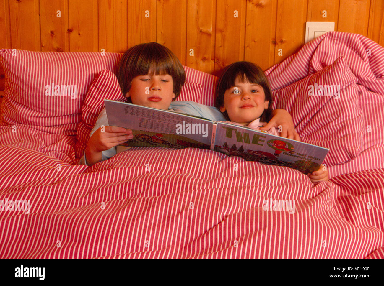 two kids reading a child book in bed. Photo by Willy Matheisl Stock Photo