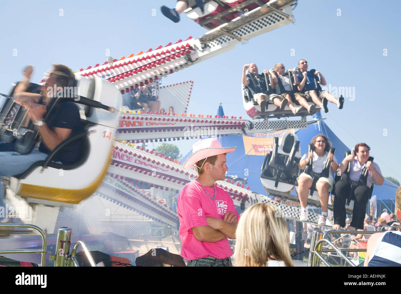 Gay Pride festival Brighton. Man in pink stetson hat stands in front of a fun fair ride showing people enjoying themselves. Stock Photo