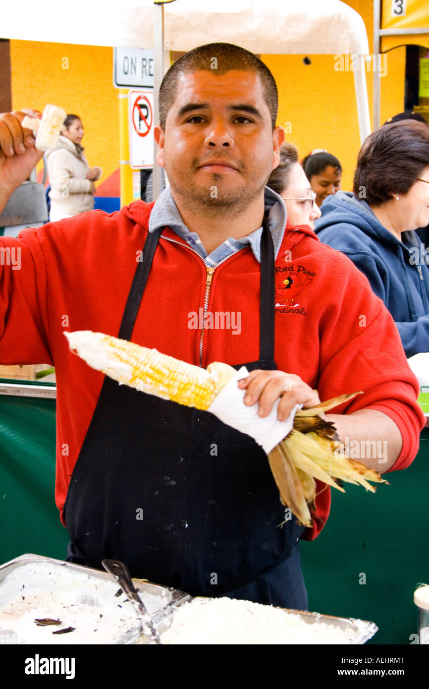 Chicano chef age 21 serving just roasted sugared corn on the cob. Cinco de Mayo Fiesta. 'St Paul' Minnesota USA Stock Photo