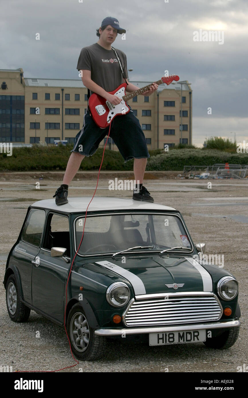 A man stands on top of a Rover Mini Cooper with a Fender Jaguar electric guitar Stock Photo