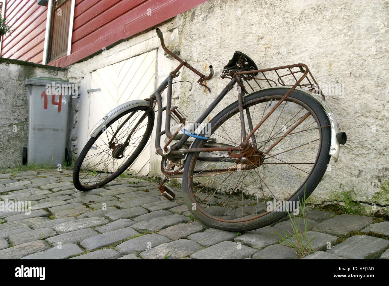 An old rusty bike leaning up against a building on a cobblestone road in Bergen Norway Stock Photo