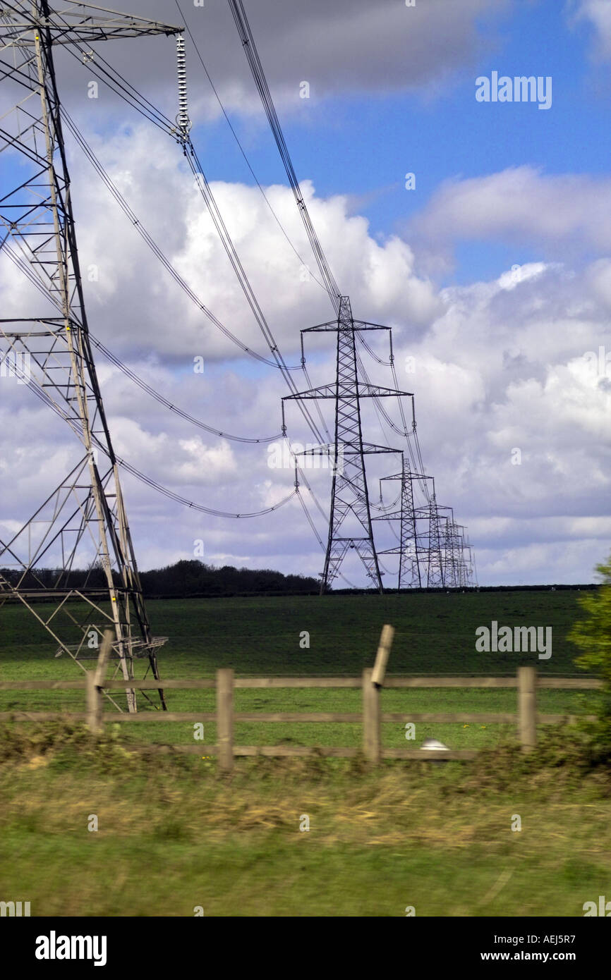 Electricity pylons receeding to horizon across green field Stock Photo