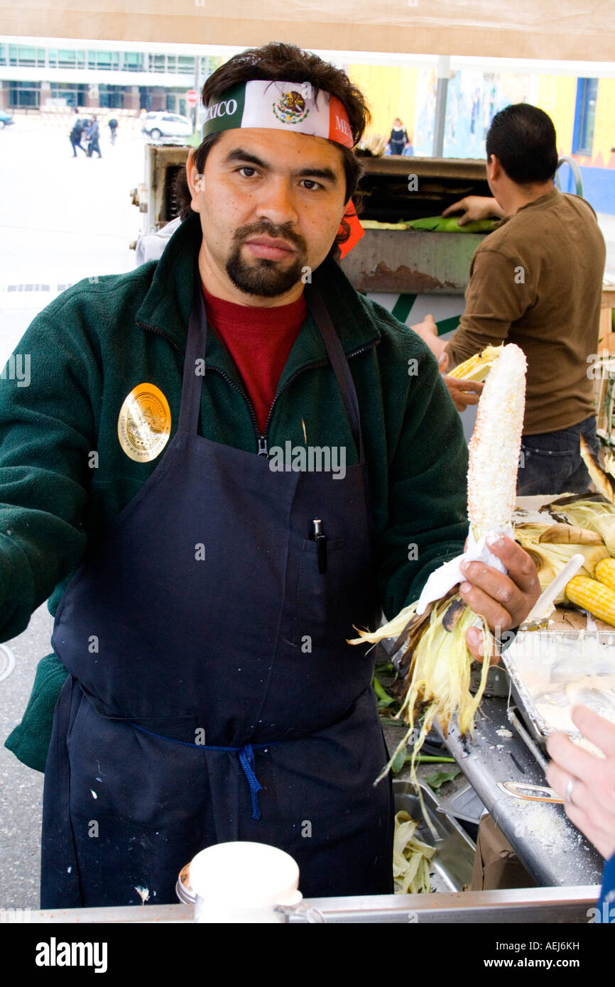 Chicano chef age 24 holds roasted corn on the cob wearing Mexican flag headband. Cinco de Mayo Fiesta. St Paul Minnesota USA Stock Photo