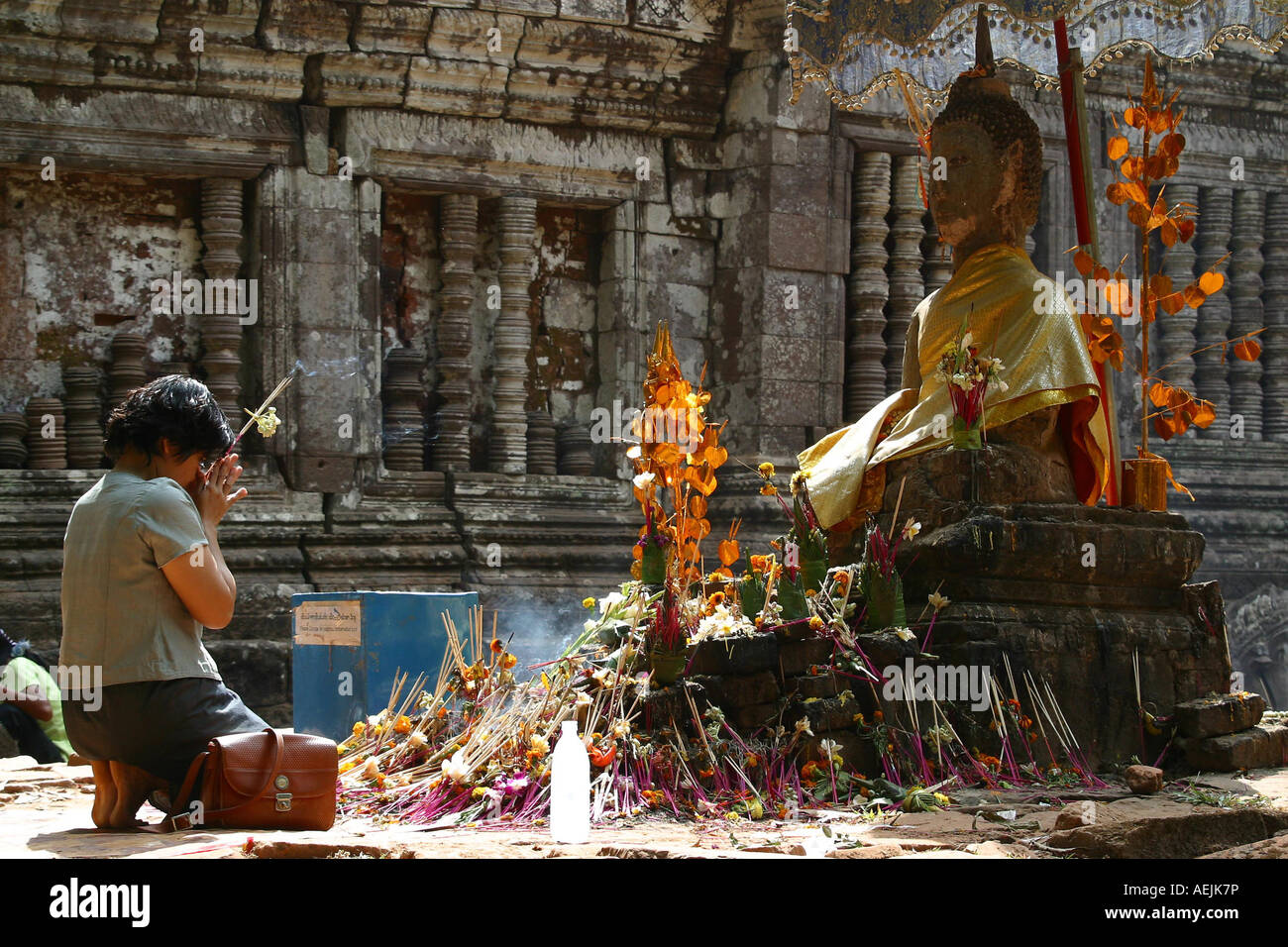 Young buddhist woman praying in front of a buddha statue at the temple Wat Phou, Wat Phou, Laos Stock Photo