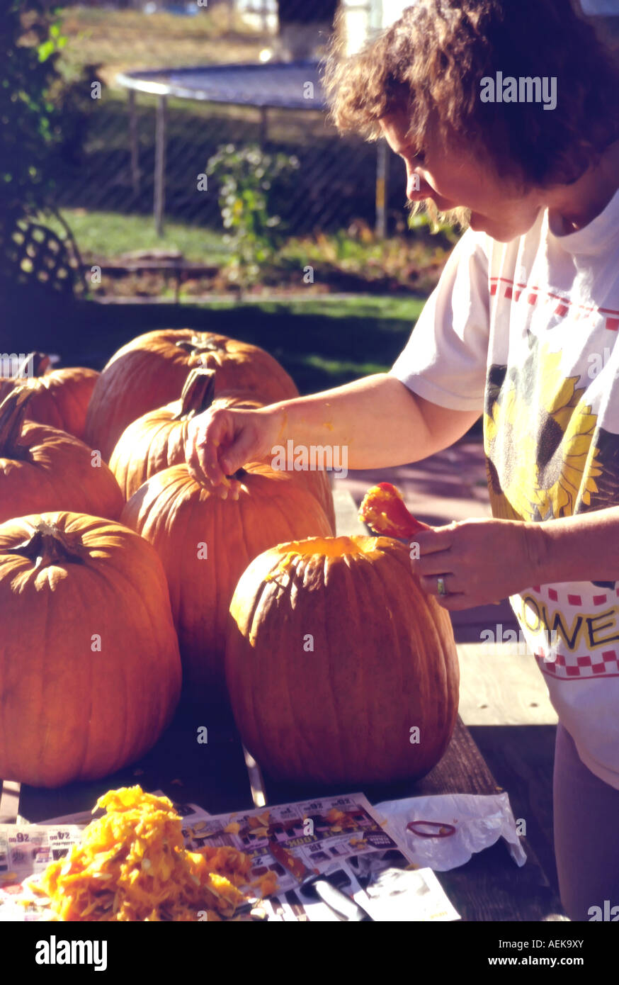 A woman cleans out several pumpkins, on an outdoor patio table, before a family carving party in Utah, USA. Stock Photo
