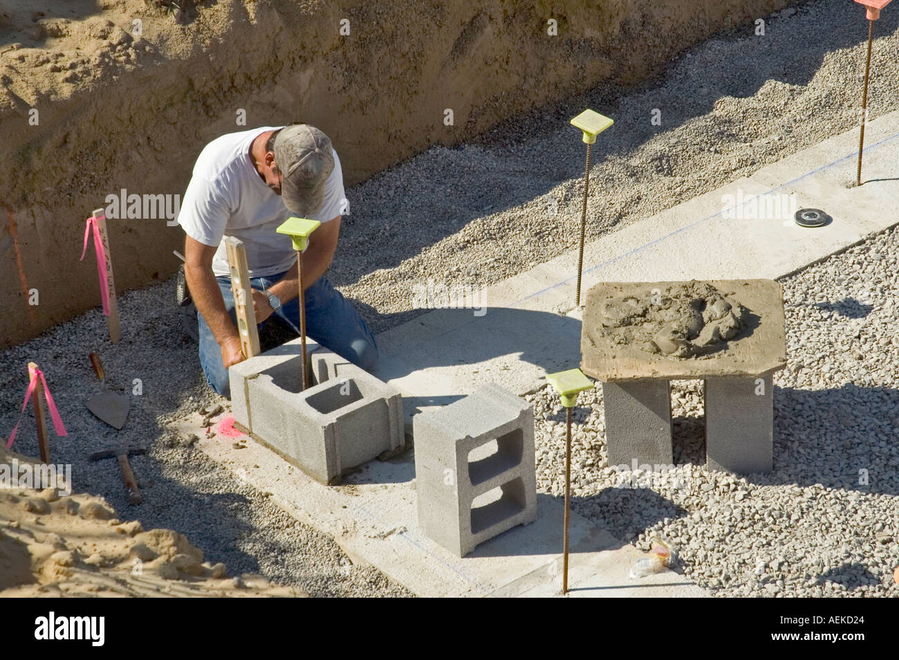 Cement workers prepare to lay brick foundation by measuring placing and leveling cinder blocks