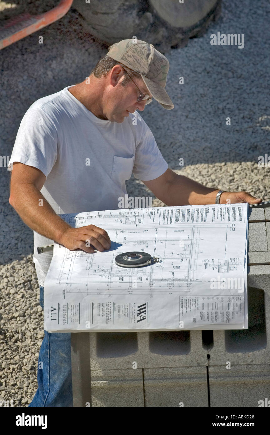 Cement workers prepare to lay brick foundation by measuring placing and leveling cinder blocks