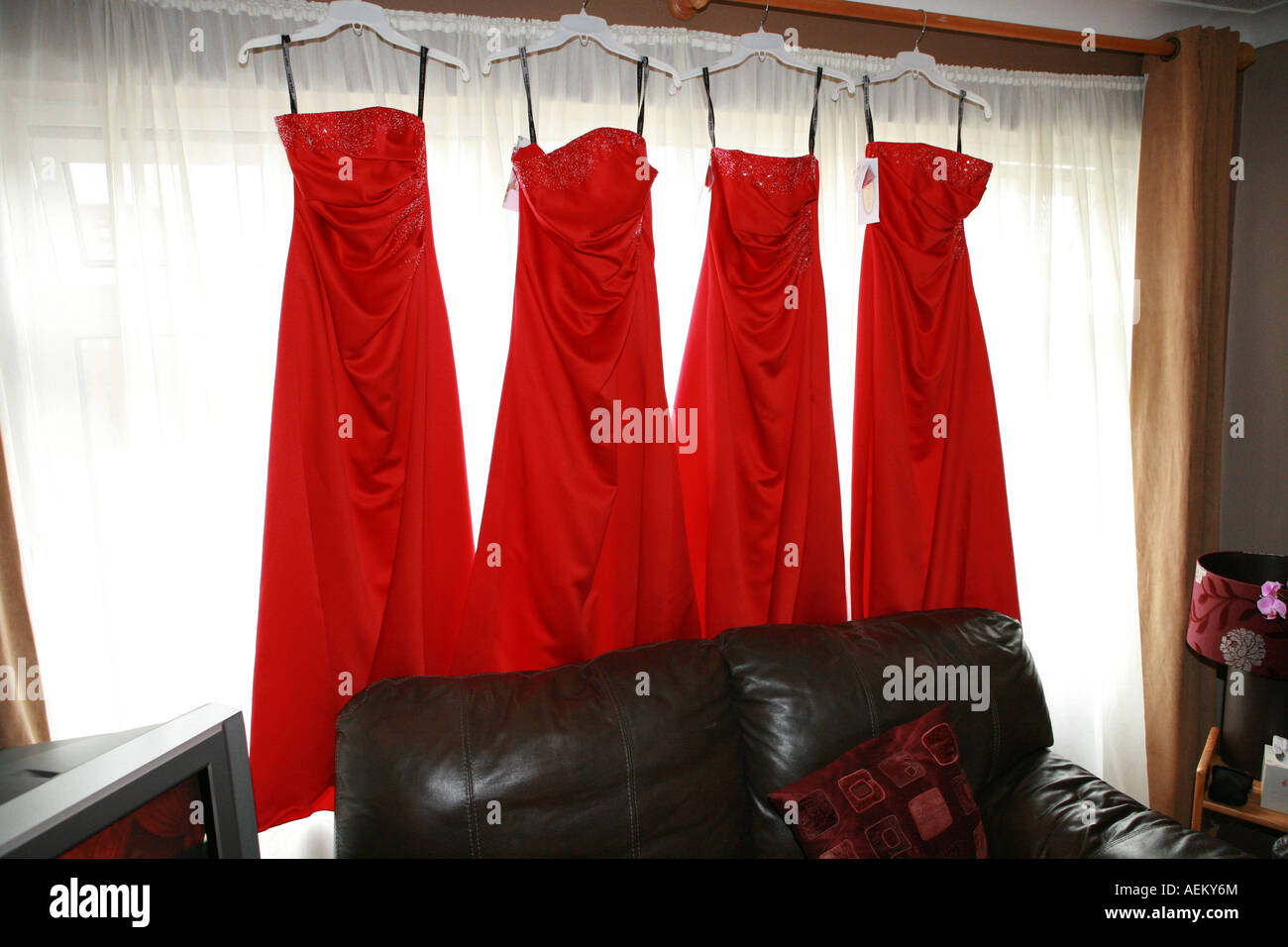Four 4 bright red brides maids dresses hanging from a window in a house on a wedding day morning UK Stock Photo