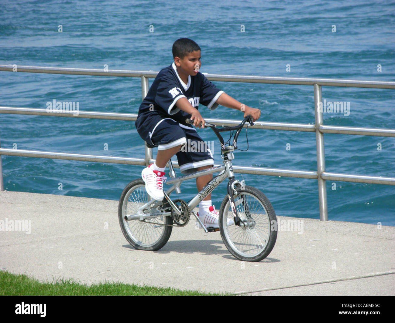 Black ethnic boy rides bicycle along rivers edge for pleasure Stock Photo