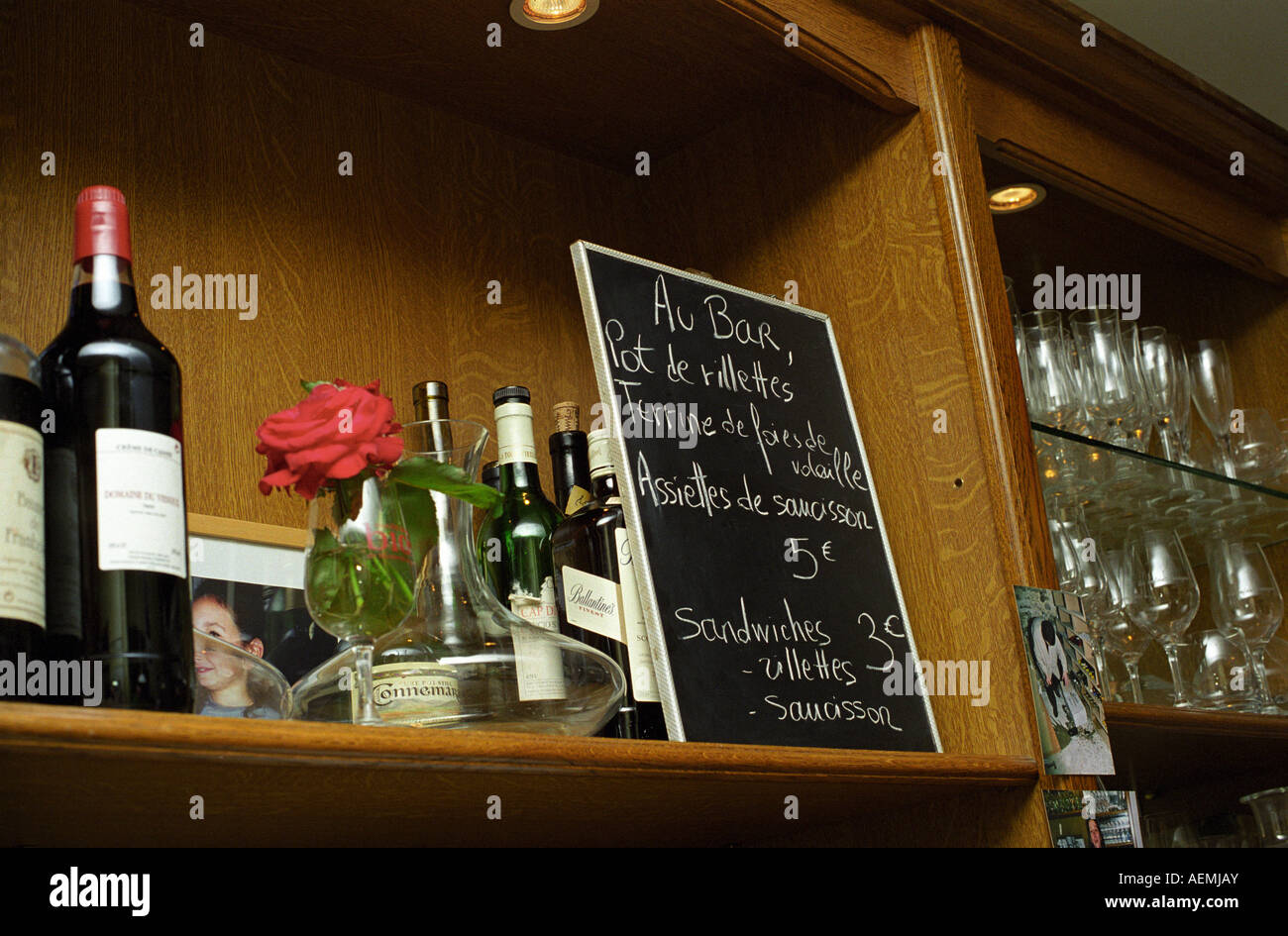 Shelf in a bar with bottles glasses flower and chalk board. Wine bar les Enfants Rouges in Paris. Paris, France. Stock Photo