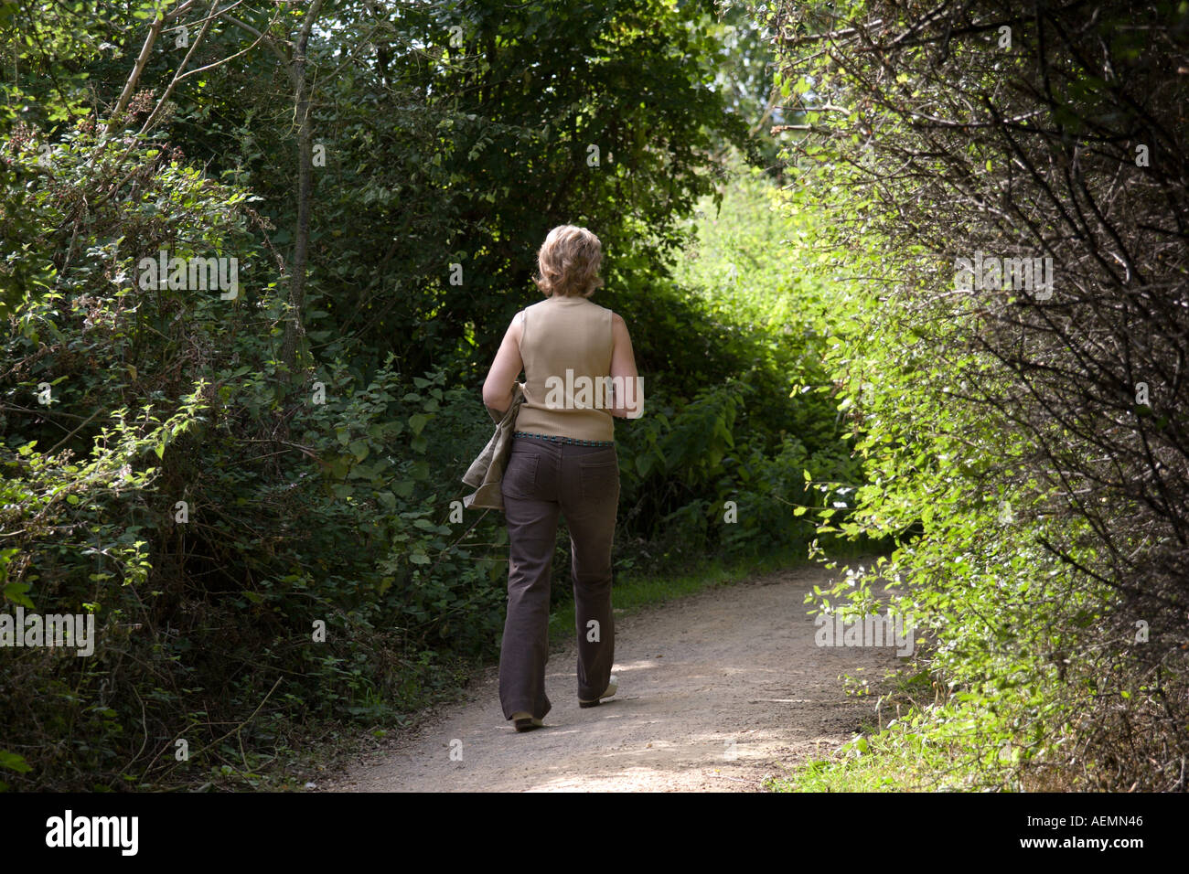 A middle aged woman walking on a lonely path on the Wivenhoe trail in the countryside Stock Photo
