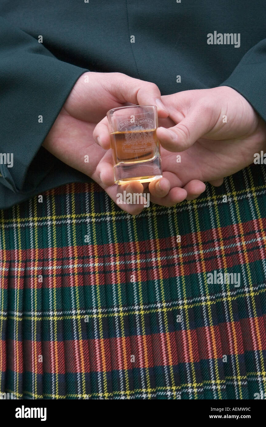 Man wearing a tartan kilt holding a glass of whisky behind his back at Braemar,  Ballater Highland Games. Stock Photo