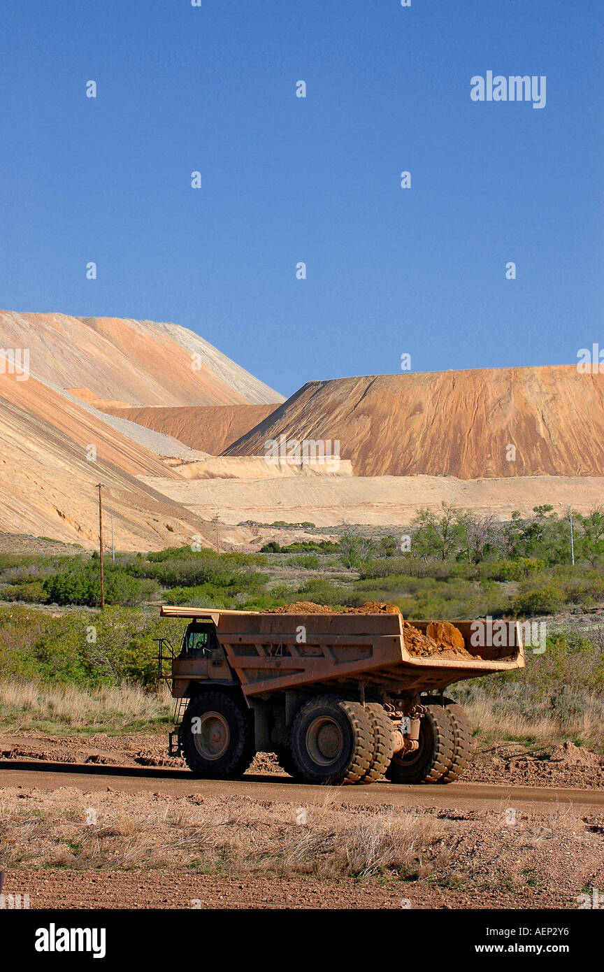 A huge dump truck drives down a dirt road dwarfed by the gigantic slag heaps in the background Stock Photo