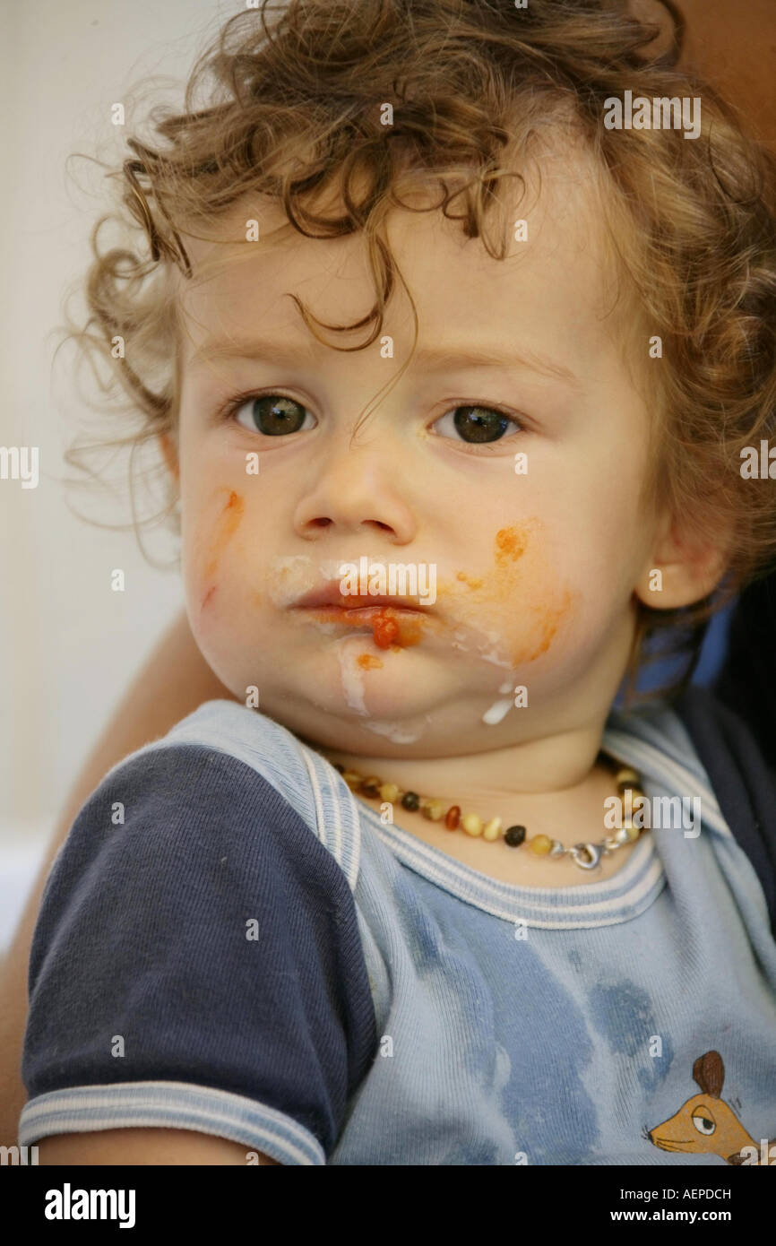 Kleinkind 18 Monate alt JONI mit Bernsteinkette um den Hals lacht nach dem Essen mit verschmiertem Gesicht Model Released Stock Photo