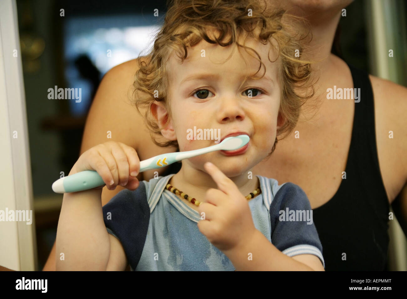 Kleinkind 18 Monate alt JONI mit Bernsteinkette putzt nach dem Essen mit verschmiertem Gesicht seine Milchzaehne Model Released Stock Photo